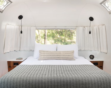 The interior of an AutoCamp airstream trailer features a cozy, neutral-colored bed with nightstands ...