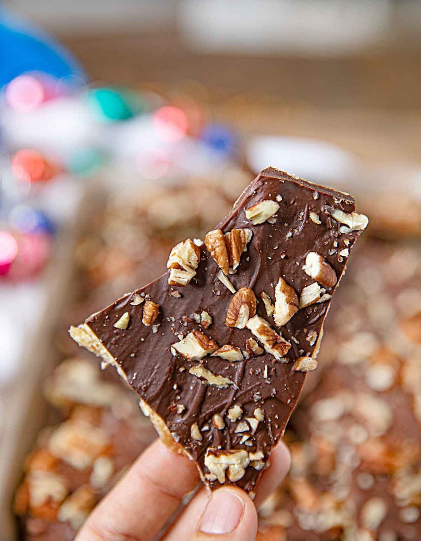 Thanksgiving sheet pan desserts, hand holding a piece of saltine toffee with walnuts