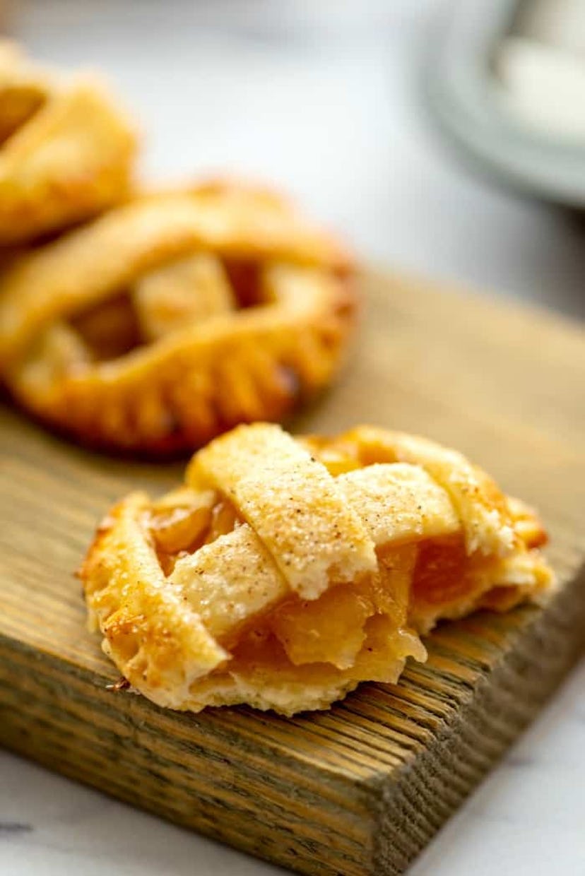 Thanksgiving sheet pan desserts, caramel apple pie cookies laying on a wooden cutting board, one coo...