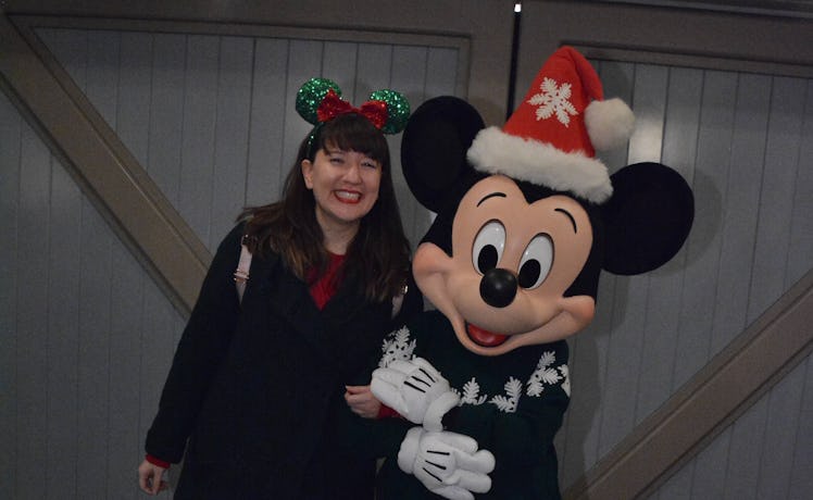 A smiling woman wearing festive red and green Minnie ears poses with Mickey Mouse at Disneyland duri...