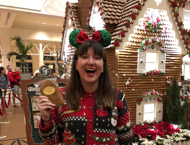A smiling woman holds a gingerbread cookie and wears a Christmas sweater and festive Minnie ears at ...