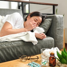 A woman with the flu lies on the couch.Vitamin c works to prevent the flu in a variety of ways.
