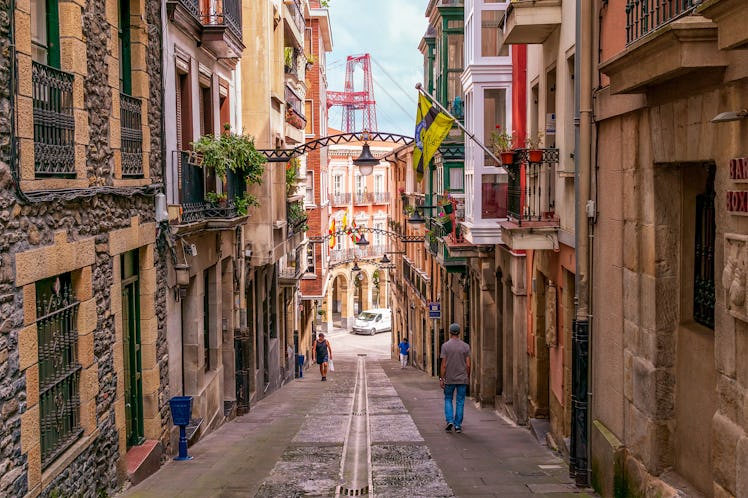 A street in Bilbao, Spain has colorful building and archways, and a view of a red bridge.