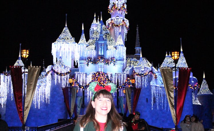 A smiling woman wearing festive Minnie ears stands in front of Disneyland's castle during the holida...
