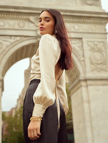 A brunette woman in a holiday outfit - a cream satin blouse and a black skirt