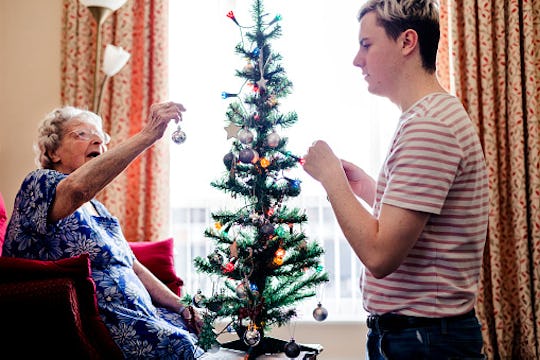 kid helping a elderly woman decorate christmas tree in a nursing home
