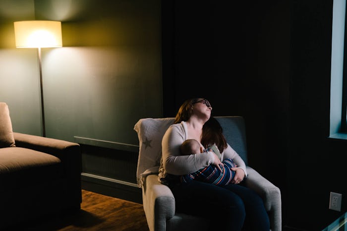 an exhausted mom breastfeeding a baby in a chair