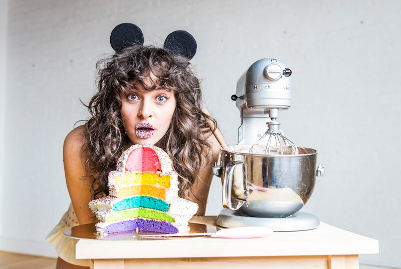 Amirah Kassem of Flour Shop poses with one of her signature rainbow cakes and a kitchenaid mixer.