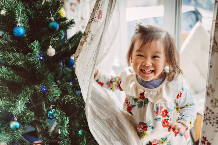 little girl hides behind curtains near Christmas tree