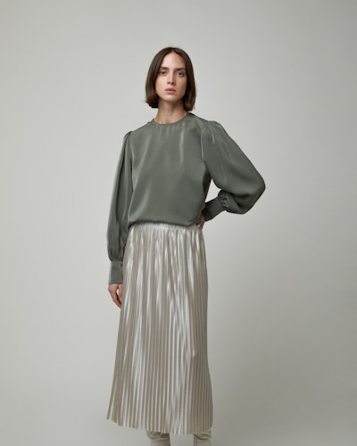 A model wearing Oak + Fort's pleated skirt and an olive-green blouse