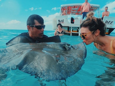 A girl in sunglasses and a bikini kisses a stingray in the water.