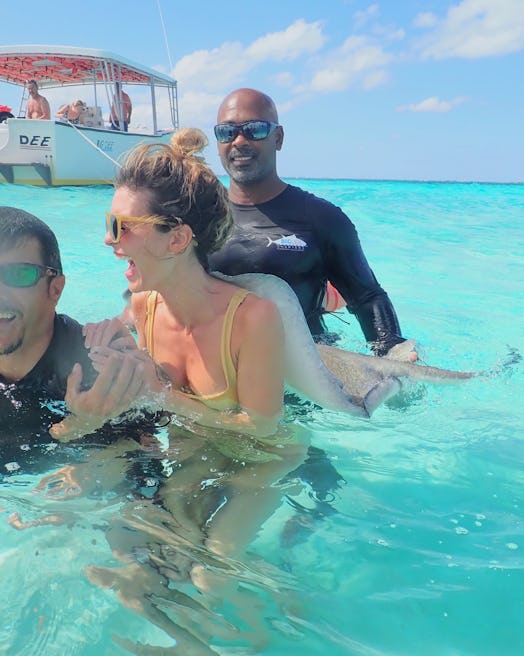 A girl in sunglasses and a bikini gets a stingray back massage in the water.