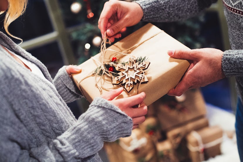 A woman and a man holding a Christmas gift together while he is unwrapping it. 