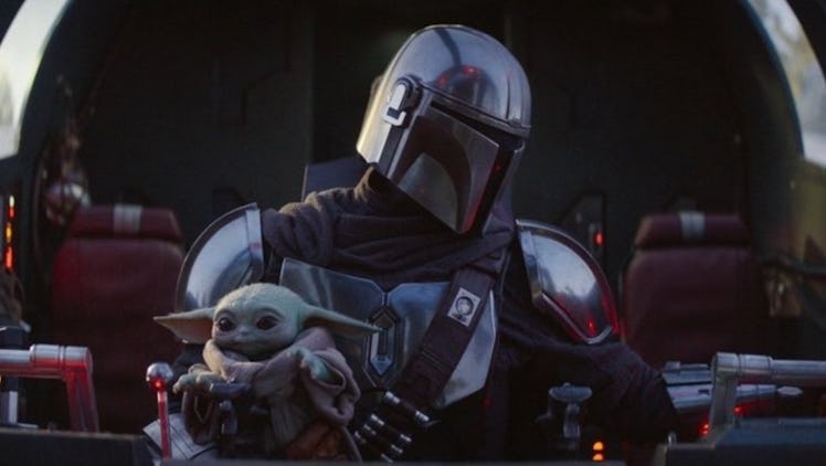 Baby Yoda sits in Mando's lap in 'The Mandalorian' while they ride in a spacecraft.