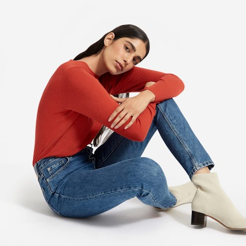 A female model posing in a red shirt, black pants, and white ankle boots