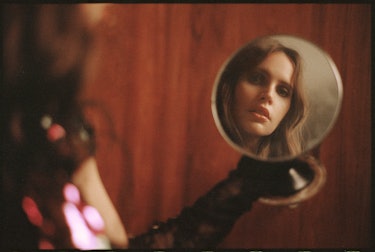 Felicity Jones holding a mirror and looking at her face while wearing black Gucci gloves
