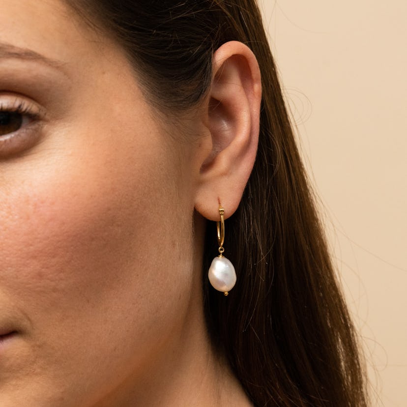 A close-up of a brunette woman's ear, wearing a pearl earring by Mejuri