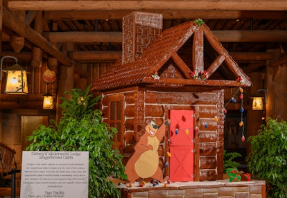 A gingerbread log cabin with a bear hanging Christmas lights is on display at Disney's Wilderness Lo...