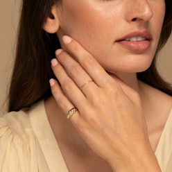 A close-up of a brunette woman's hand on her chin, wearing two Mejuri rings