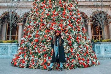 A travel blogger poses in front of the Christmas tree at Lotte New York Palace in a wintertime outfi...