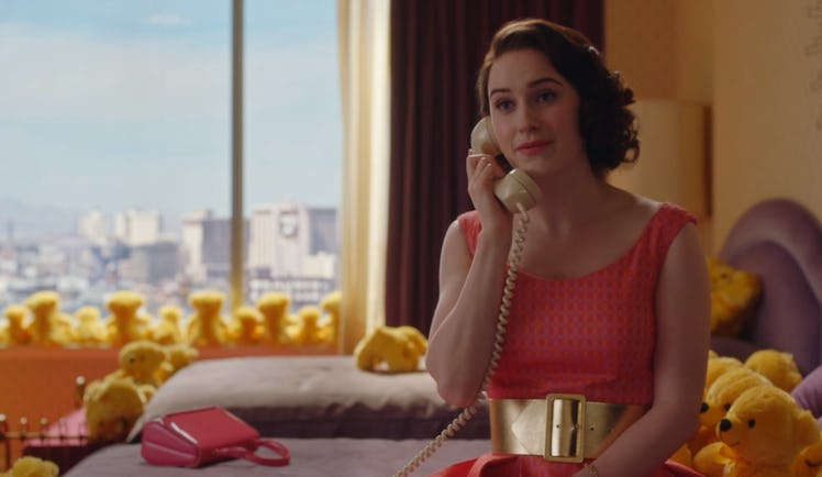 A scene from 'The Marvelous Mrs. Maisel" where Midge sits on a bed in a pink dress and is surrounded...