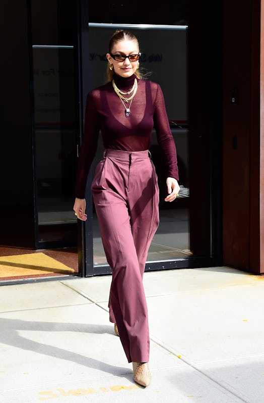 Model Gigi Hadid wear a sheer cranberry turtleneck sweater and coordinating trousers with chunky gol...