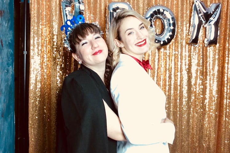 Two friends smile and pose for a New Year's Eve photo in a glittery photo booth. 