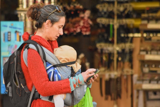 mom checks phone while walking with baby in carrier