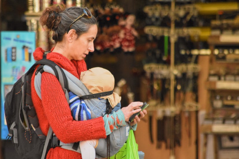 mom checks phone while walking with baby in carrier