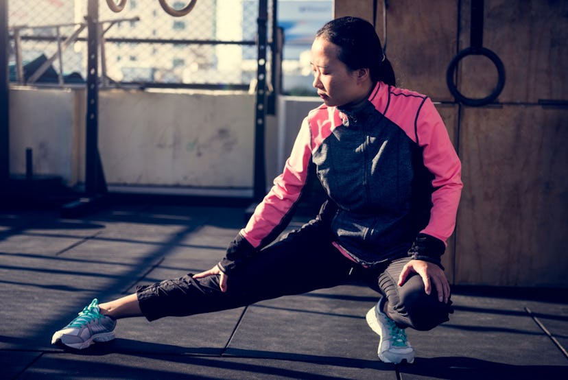 A person in a blue and pink workout jacket stretches on the gym floor. Having goals about your body ...
