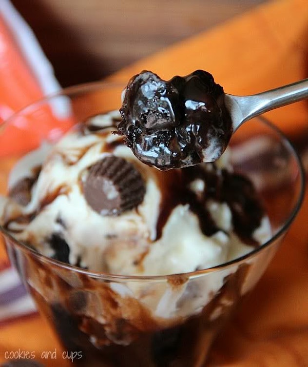 spoon scooping gooey chocolate cake from glass cup topped with ice cream and chocolate syrup