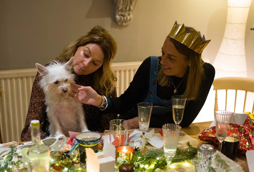 Two friends sitting with a dog at a Christmas decorated table
