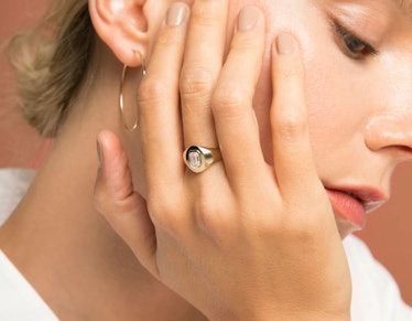 A model holding her hand to her face highlighting both the ring on her finger as well as her hoop ea...