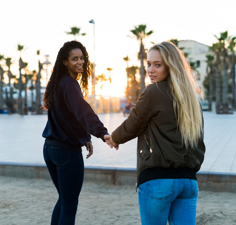 Two young women holding hands at sunset, showing the meaning of twin flame.