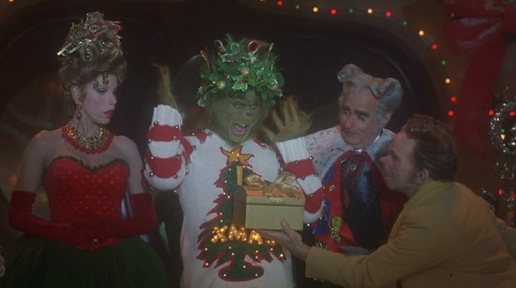 The Grinch from 'Dr. Seuss' How The Grinch Stole Christmas' wears a festive sweater and opens a pres...