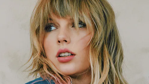 Taylor Swift with her long blonde hair and bangs looking on the side