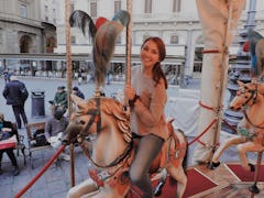 A girl wearing jeans and a sweater smiles on a carousel in Florence, Italy around the holidays.