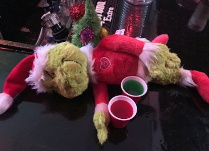 A 'Grinch' plush toy lays on a bar next to red and green Jello shots at a holiday pop-up experience ...