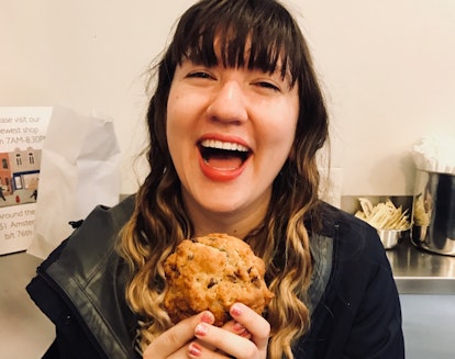 A happy woman holds a chocolate chip cookie and smiles.