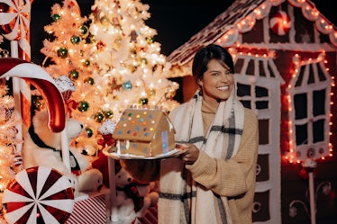 A woman smiles and holds up a gingerbread house at Santa's North Pole Village in LA. 