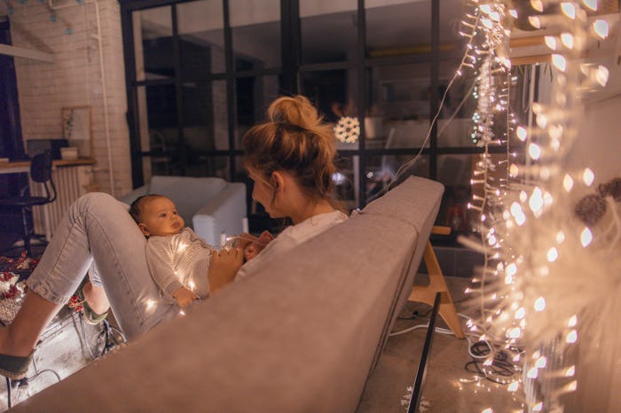 a mom holds a newborn by a christmas tree