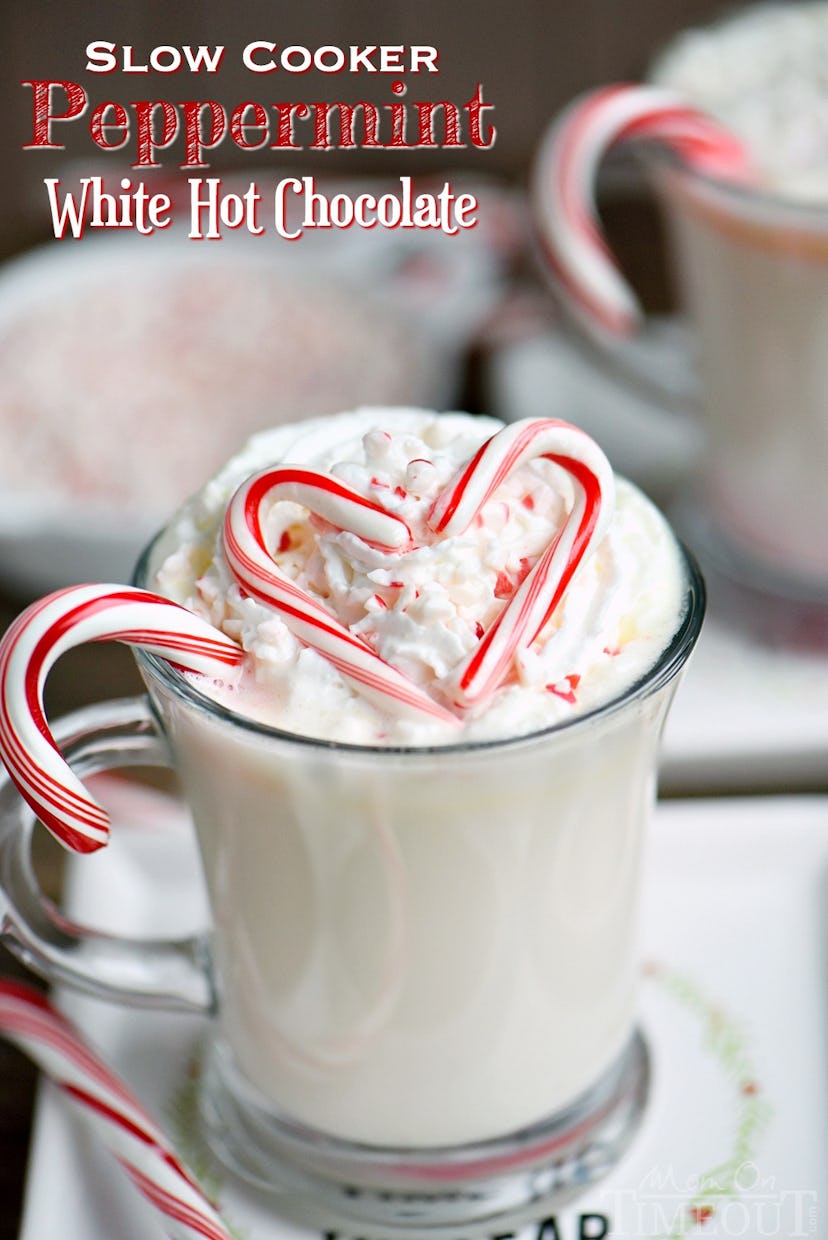 glass mug of white hot chocolate with whipped cream and candy canes in shape of a heart on top 