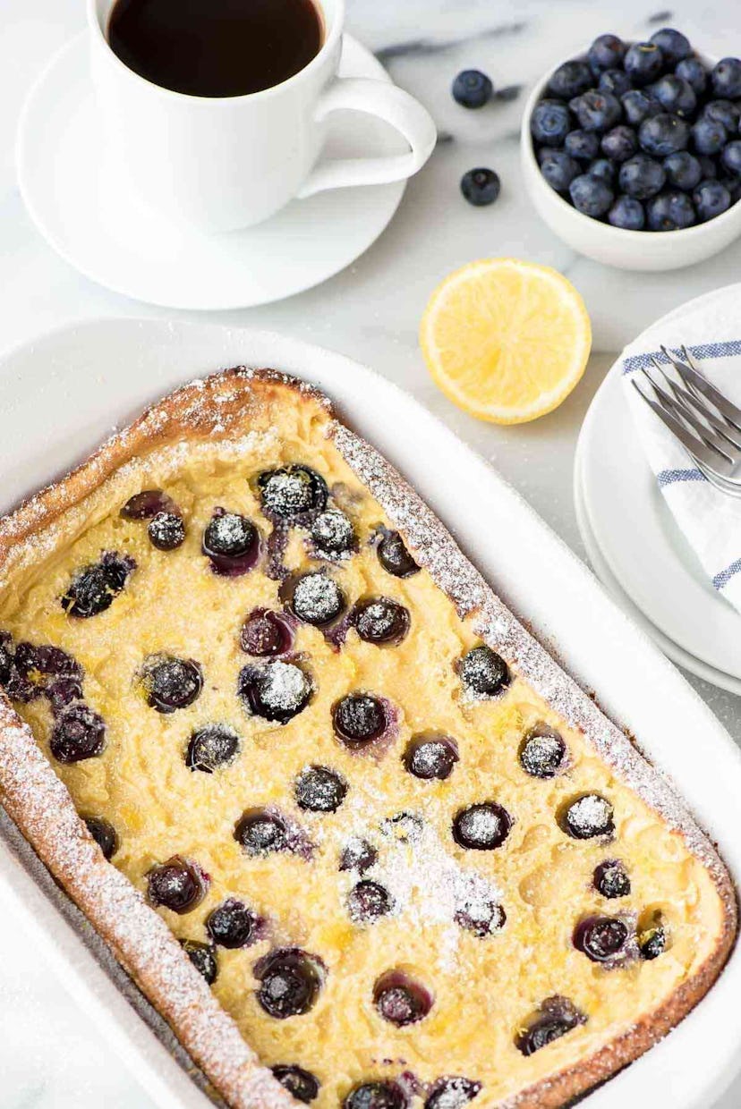 white dish pan with large pancake with blueberries in it sprinkled in powdered sugar.