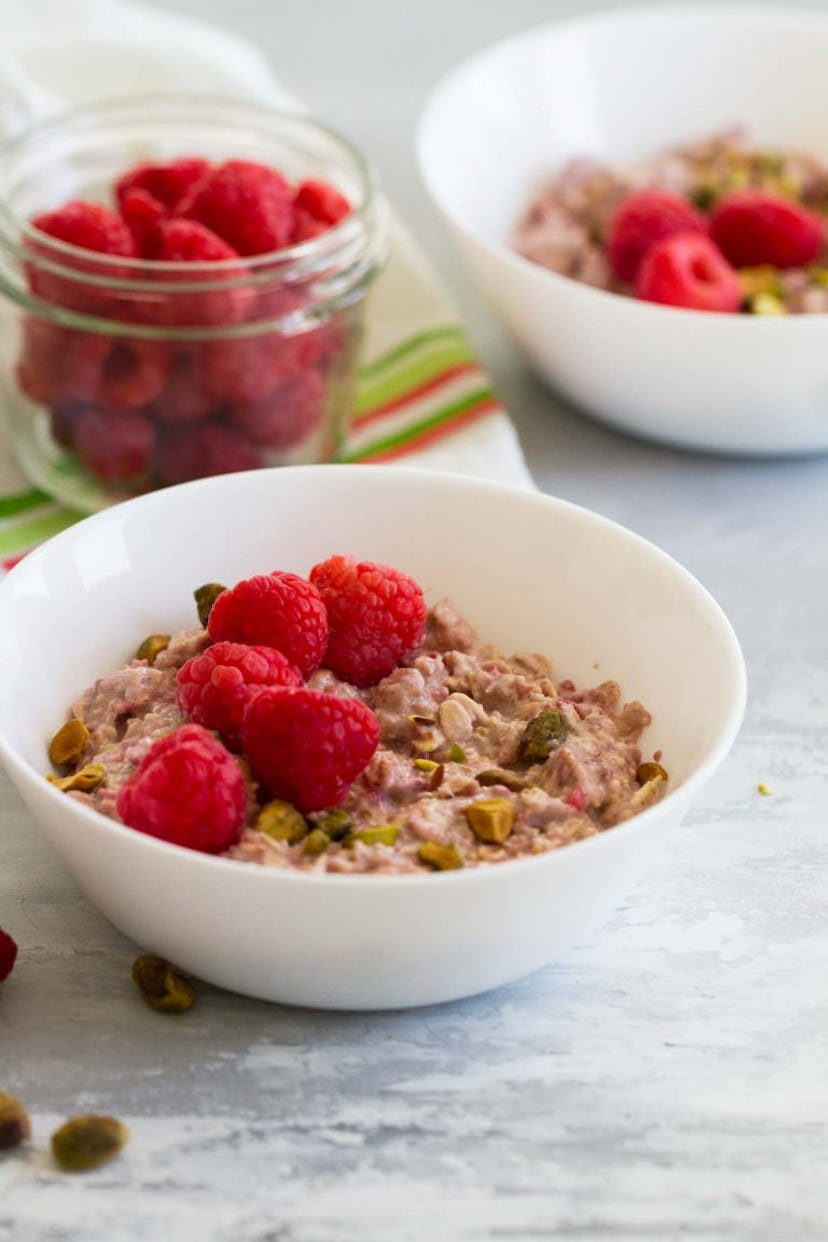 two white bowls of oats in yogurt with pumpkin seeds and raspberries on top