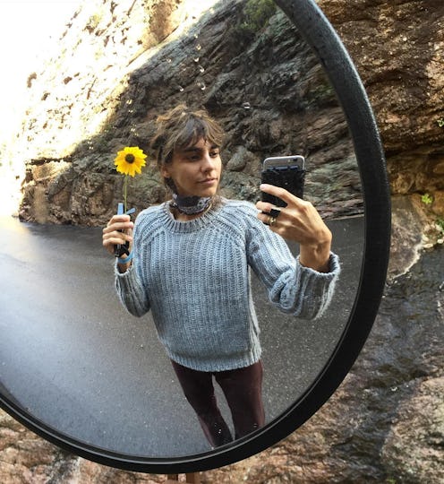Mari Giudicelli taking a selfie in a curved mirror while holding a small sunflower