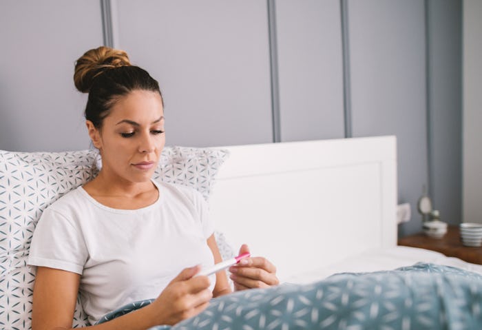 a woman in bed reading a pregnancy test