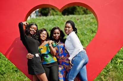 A group of women pose in front of a heart-shaped art installation outside on a sunny day.