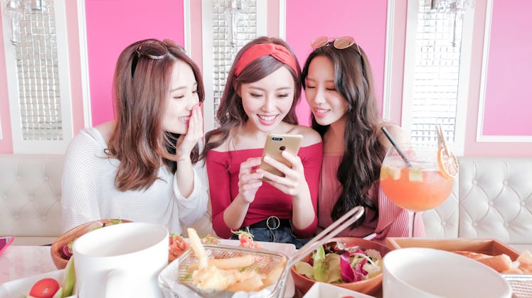 Three girls smile while looking at a cell phone at brunch.