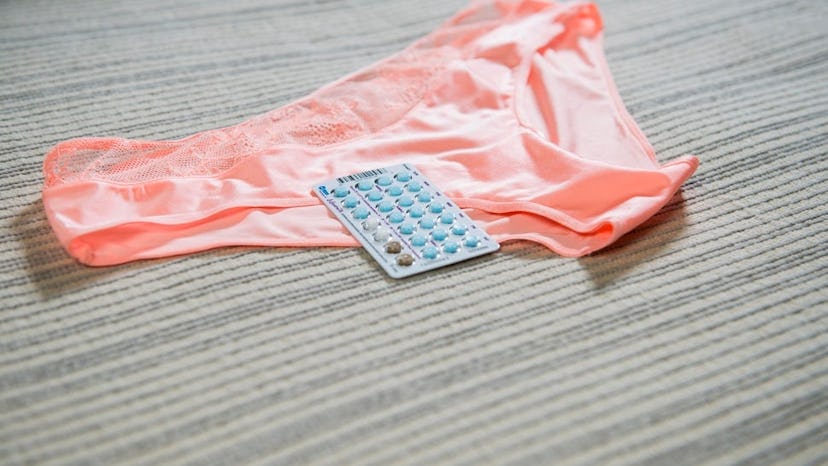 Birth control pills placed on peach-colored underwear