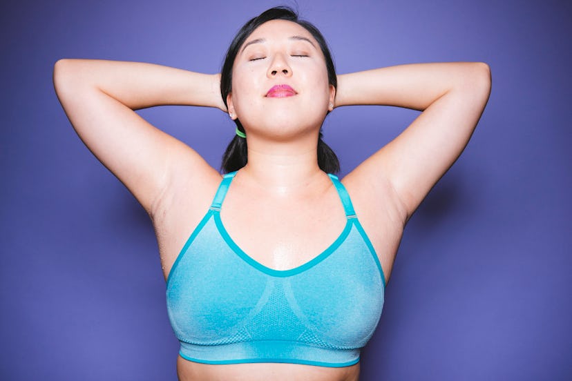 A woman stretching her neck, shoulders, and elbows in a blue sports bra